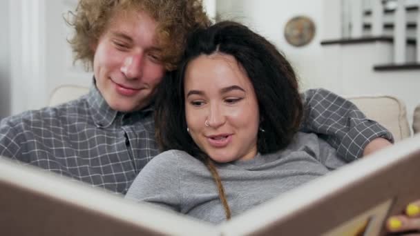 Nahaufnahme attraktiver amortisierter glückliches junges Paar sucht Fotoalbum auf der Couch im Wohnzimmer — Stockvideo