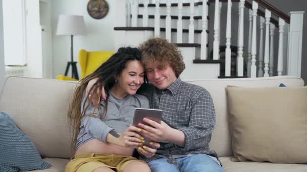 Очаровательная романтичная супружеская пара преганат влюбленных, сидящая на мягком диване в гостиной и смотрящая фото на i-pad — стоковое видео