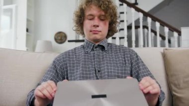 Ev bilgisayarında çalışmaya başlayan kıvırcık saçlı yakışıklı, kendine güvenen genç ofis çalışanının ön görüntüsü.