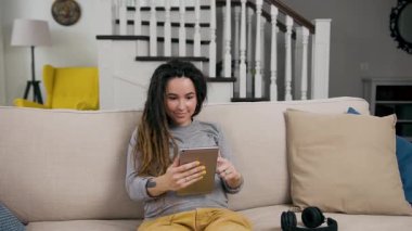 Çekici, güler yüzlü, şık, hamile bir kadın oturma odasındaki rahat koltukta oturuyor ve i-pad 'de en sevdiği uygulamaları izliyor.