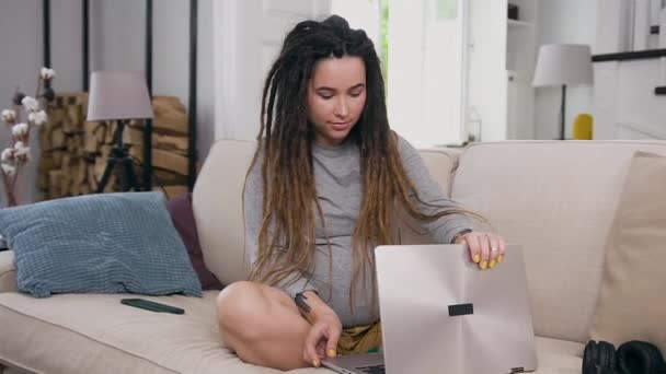 Счастливая улыбающаяся молодая замужняя беременная женщина с мечом сидит на мягком диване в современной квартире и разговаривает с подругой во время видеочата с помощью компьютера — стоковое видео