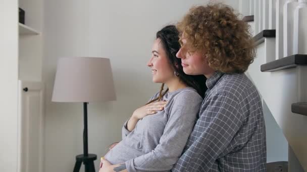 Nahaufnahme von attraktiven glücklichen jungen verheirateten Schwangeren, die am großen Fenster stehen und ihren Bauch sanft streicheln — Stockvideo