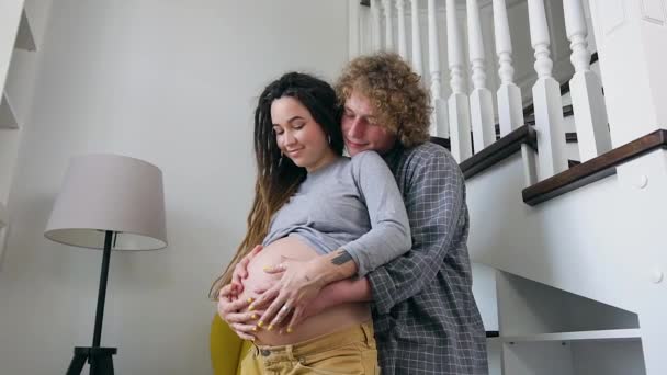 Gros plan de beau couple marié heureux souriant enceinte amoureux qui se tient devant la fenêtre et toucher tendrement son ventre avec le futur bébé — Video
