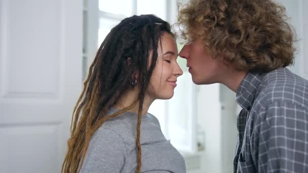 Bonito jovem homem encaracolado feliz beijando no nariz sua esposa grávida na moda sorridente e gentilmente tocando sua barriga, close-up — Vídeo de Stock