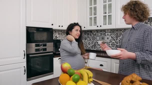 행복 한 미소를 짓고 있는 부부의 매력적 인 모습: 곱슬곱슬 한 남편이 드레드 머리와 매력적 인 임산부를 위해 아침 식사를 준비하고 있는 현대 주방에 있는 부부 — 비디오