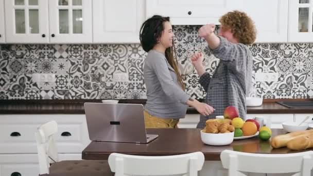 Закройте привлекательную счастливую улыбчивую беременную пару, которая наслаждается совместным танцем на кухне, а затем целуется друг с другом — стоковое видео