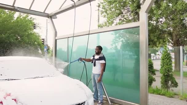 Concentrado barbudo bem parecido afro-americano lavar seu carro com espuma seca usando arruela de alta pressão na lavagem de carro self-service — Vídeo de Stock