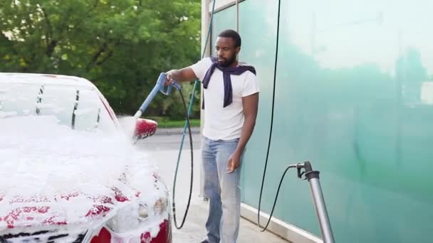 Close up de boa aparência moderna jovem afro-americana com barba que lavar o carro na lavagem de carros ao ar livre usando tubo de jato com espuma — Vídeo de Stock