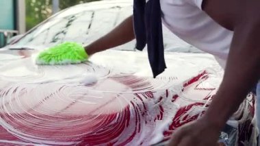 Araba yıkama istasyonunda köpük temizleyen eldiven ile araba kaputunu yıkayan yakışıklı Afro-Amerikan 'ın ön görüntüsü.