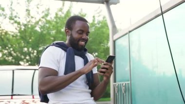 Yakışıklı, mutlu, sakallı, esmer tenli adam araba yıkama ve telefon uygulamalarında arabasının yanında duruyor.