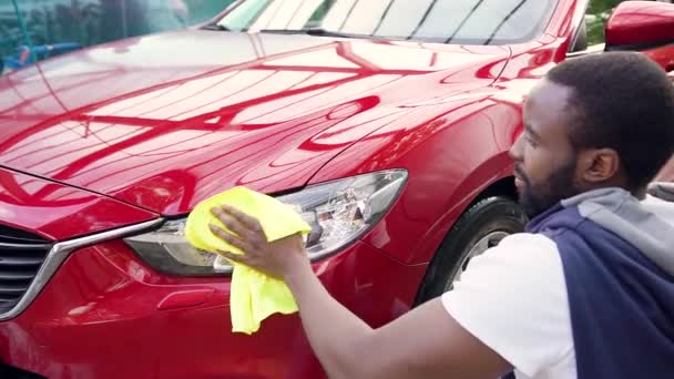 Guapo seguro joven barbudo afroamericano pulido con trapo de microfibra sus propios faros de coches en el lavado de coches — Vídeos de Stock