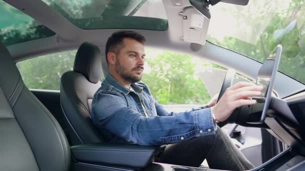 Привабливий концентрований молодий бородатий чоловік у стильному одязі, що сидить всередині свого розкішного автомобіля та використовує навігатор GPS — стокове відео