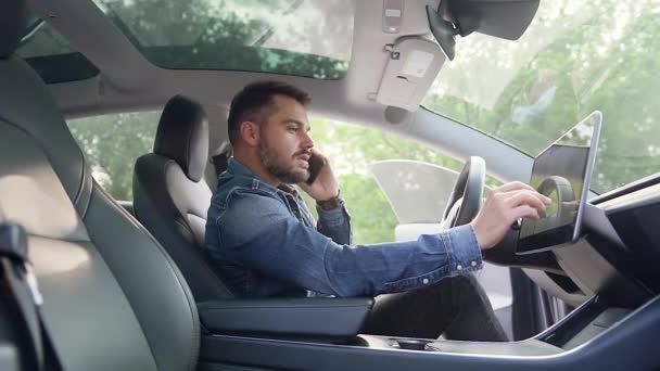 Chico joven barbudo positivo agradable en ropa elegante disfrutando de su conversación móvil en el manillar de su propio coche y el uso de navegador, vista lateral — Vídeo de stock