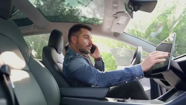 Ελκυστικός συμπυκνωμένος γενειοφόρος σύγχρονος άνδρας κάθεται στο τιμόνι του ακριβού αυτοκινήτου του, μιλώντας στο κινητό και χρησιμοποιώντας GPS πλοηγός, κοντινό πλάνο — Αρχείο Βίντεο