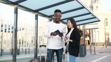 Hoş, gülümseyen, sakallı, esmer bir adam otobüs durağında yan yana duruyor. Tatmin olmuş Asyalı kız arkadaşıyla biletlere bakıyor.