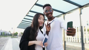 Çekici, neşeli, çoklu etnik çeşitlilikte iki arkadaş, tramvay durağında cep telefonu konuşmalarında el sallayarak ortak dostlarını selamlıyor.