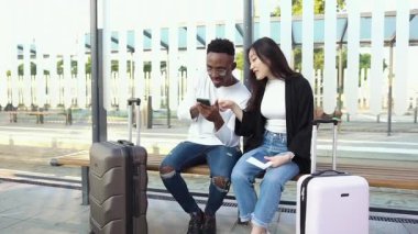 Seyahat konsepti, tramvay ya da otobüs durağında oturan yakışıklı, gülümseyen, melez genç ırk arkadaşlarının, ulaşım için bekledikleri ve telefon kullandıkları yer.