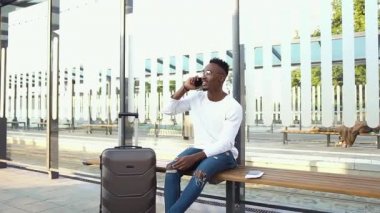 Sempatik gülümseyen sakallı Afro-Amerikalı gözlüklü otobüs ya da tramvay durağında bekliyor ve cep telefonuyla olumlu bir konuşma yapıyor.