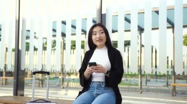 Güzel, rüya gibi, genç Asyalı kadın, günlük giysiler içinde toplu taşıma aracında oturuyor. Akıllı telefon, ön görüş kullanıyor.