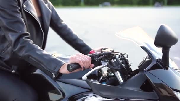 Joven motorista esbelta irreconocible en ropa de cuero elegante sentada en una motocicleta deportiva negra en un terreno deportivo — Vídeo de stock