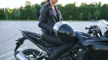 Oldukça kendine güvenen, şık, genç esmer, atkuyruklu, siyah moda elbiseli, spor sahasında lüks bir motosiklette oturan...