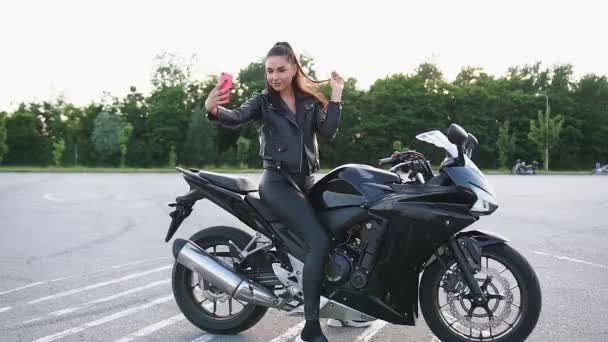 Güzel, mutlu, güler yüzlü, modaya uygun, siyah elbiseli, lüks motosiklet üzerinde oturan ve selfie çeken bir bayan motorcu. — Stok video