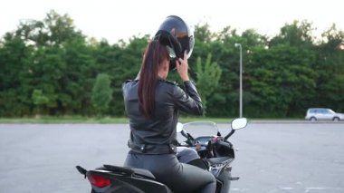 Meçhul, şık, zarif, motosikletli, deri elbiseli bir kadın lüks bir motosikletin üzerinde oturuyor ve koruyucu bir kask takıyor.