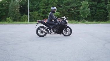 Çekici, kendine güvenen, zarif, kask takan, spor sahasında lüks siyah motosikletli bir kadının ön görüntüsü.