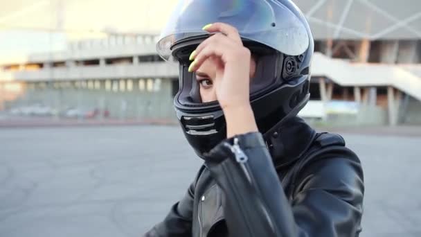 Preciosa mujer joven elegante y segura de sí misma en casco negro mirando a la cámara, sentado en la motocicleta deportiva negro, vista redonda — Vídeo de stock