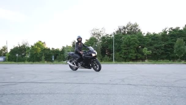 Schöne selbstbewusste schlanke, stylische junge Frau mit Schutzhelm in schwarzer Kleidung auf schwarzem, sportlichem Motorrad auf Mototrack — Stockvideo