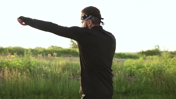 Gut aussehender, konzentrierter junger, sportlicher, bärtiger Mann in schwarzer Sportbekleidung, der vor laufender Kamera Boxschläge macht, während er im Hintergrund der Natur trainiert — Stockvideo