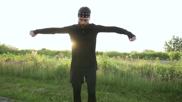 Vista frontal de belo desportivo jovem barbudo ativo em sportswear que amassar os braços enquanto treina sobre a natureza — Vídeo de Stock