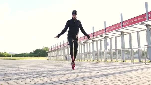 Przystojny sportowy młody brodaty facet w sportowej odzieży skaczący ze skakanką podczas treningu na specjalnej pokrywie stadionu — Wideo stockowe