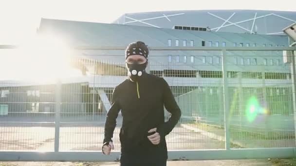 Nahaufnahme eines gut aussehenden, fitten jungen Athleten in schwarzer Sportbekleidung und Schutzmaske, der auf dem modernen Stadion läuft — Stockvideo