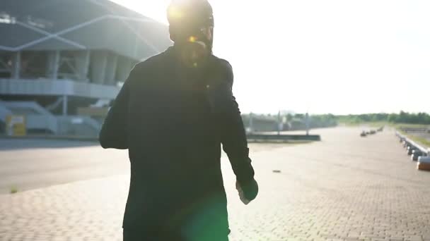 Achteraanzicht van onbekende goed uitziende actieve man in sportkleding en zwart masker die 's morgens op de runstrack van het moderne stadion loopt — Stockvideo