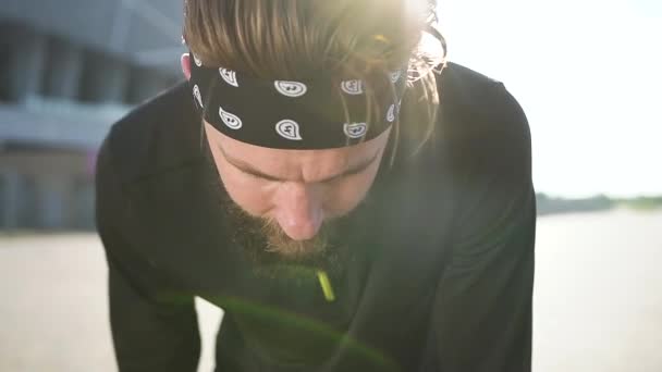 Detailní záběr atraktivní unavený silný mladý vousatý muž ve sportovním oblečení, které otírá pot a obnovení jeho dýchání po napájení venku cvičení — Stock video
