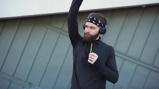Knappe zelfverzekerde sportieve actieve 35-jarige bebaarde man in sportkleding die handsfree oefeningen doet tijdens het sporten in de buitenlucht en muziek luistert op een hoofdtelefoon — Stockvideo