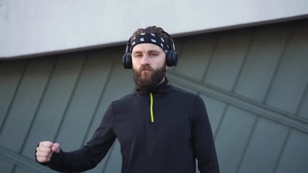 Goed uitziende sportieve jonge bebaarde man met koptelefoon die op camera zijn sterke handen laat zien als gevolg van training, close-up — Stockvideo
