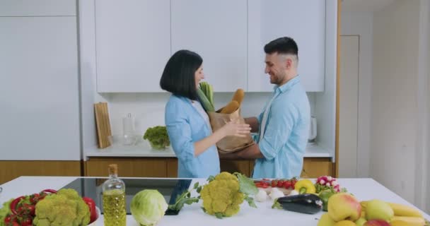 Μπροστά άποψη της όμορφη χαρούμενα νέους ανέμελη παντρεμένο ζευγάρι που διασκεδάζουν μαζί κατά τη διάρκεια της μαγειρικής στη σύγχρονη κουζίνα — Αρχείο Βίντεο