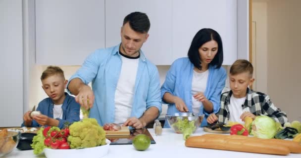 Adorabile amichevole sorridente famiglia di genitori e due figli preparare insieme deliziosa cena con verdure e carne sulla cucina moderna — Video Stock