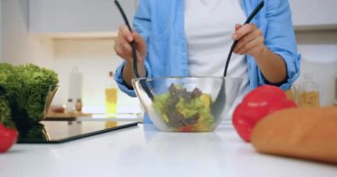 Kadın elinin önü. Kahvaltı için cam kasede sebze salatası karıştırıyor. Ya da modern mutfakta akşam yemeği.