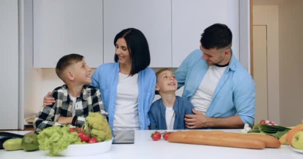 Adorabile felice sorridente amichevole coppia sposata ei loro figli in posa sulla macchina fotografica in bella cucina moderna, vista frontale — Video Stock