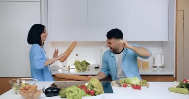 Привлекательная юная супружеская пара веселится на современной кухне во время приготовления ужина, закрыть — стоковое видео