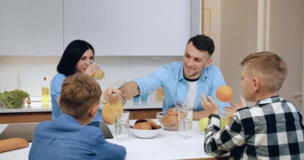 Gelukkig goed uitziende vriendelijke familie zitten rond keukentafel en ontbijten in de ochtend, vooraanzicht — Stockvideo