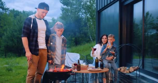 Rodzinny wypoczynek koncepcja gdzie dobroduszny uroczy szczęśliwych rodziców i dzieci gotowanie grill party na świeżym powietrzu w pobliżu własnego domu — Wideo stockowe
