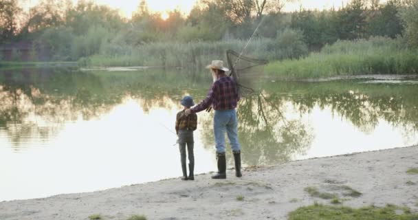Grand-père à barbe grise expérimenté et petit-enfant obéissant debout avec des palangres de pêche ensemble sur la rive des étangs, vue de dos — Video