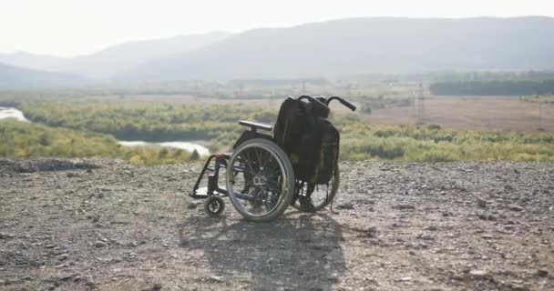 Κοντινό πλάνο του αναπηρικού αμαξιδίου με σακίδιο πλάτης που στέκεται στο λόφο στην υπέροχη φύση backround — Αρχείο Βίντεο