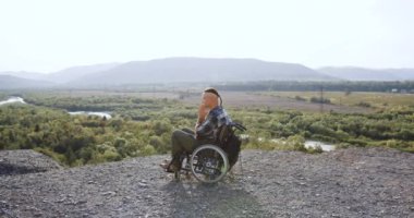 Tekerlekli sandalyedeki dengeli yakışıklının yan görüntüsü hastalıktan sonra veya kazadan sonra tepenin üstünde dua eden harika bir doğa geçmişi olan