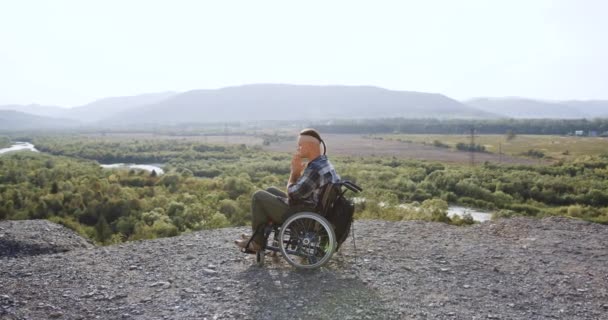 Vista lateral do homem bonito deficiente equilibrado em cadeira de rodas após a doença ou acidente que orando na colina sobre o maravilhoso fundo da natureza — Vídeo de Stock