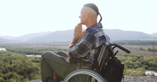 휠체어에 앉아 있는 정신적으로 잘생긴 남자의 모습을 클로즈업 해 질 때 매력적 인 배경에서 기도로 손을 펼치는 — 비디오